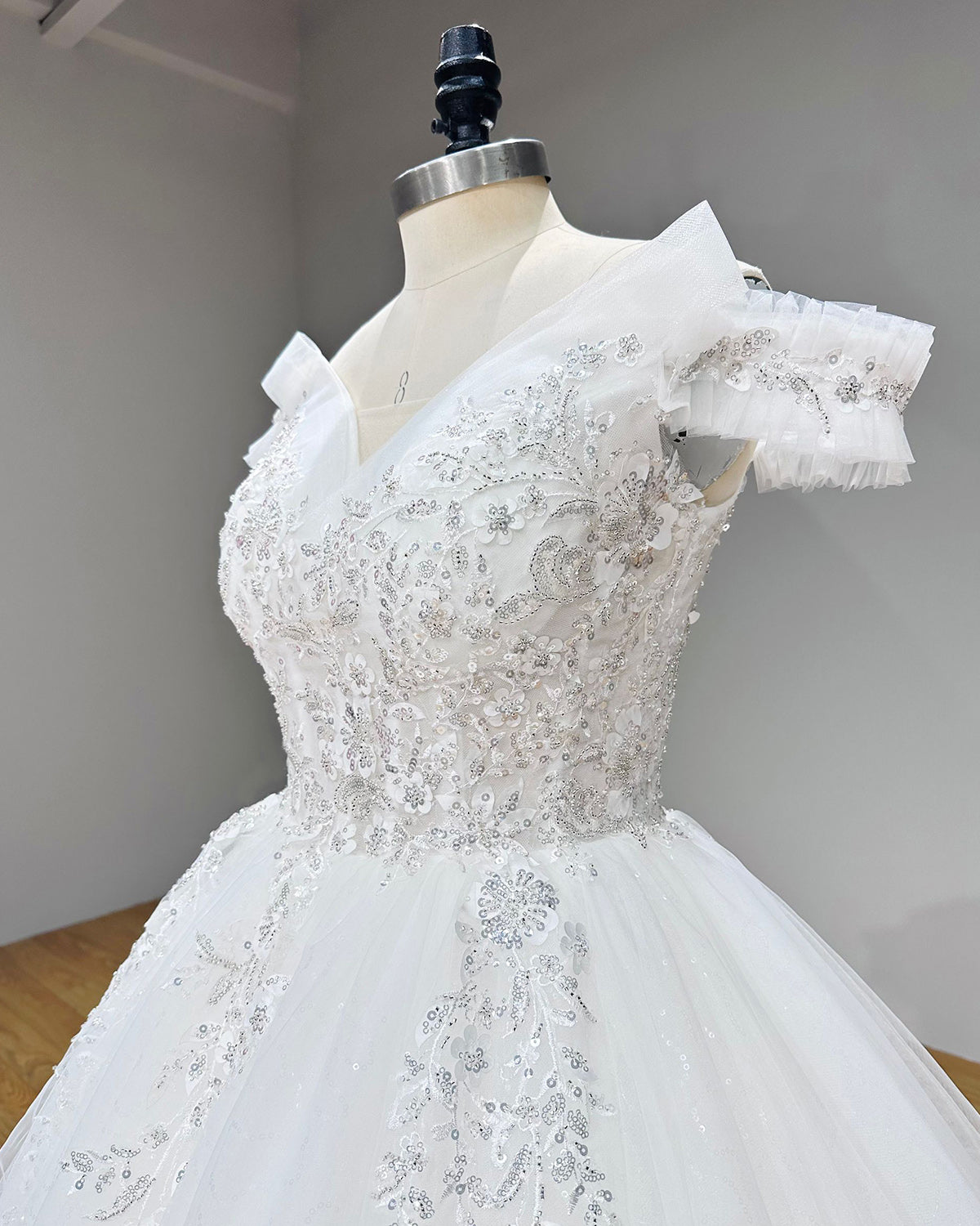 Side profile close-up of a couture wedding gown bodice detailing glamorous silver thread embroidery, floral lace sequins, and crystal bead clusters.