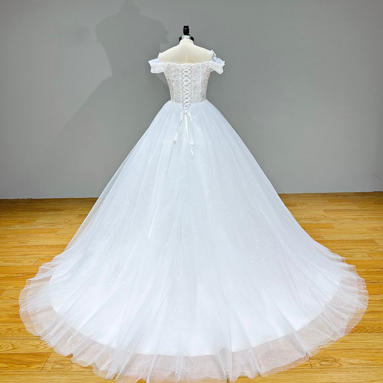Full-length back studio view of a white glitter tulle princess dress, displaying a classic lace-up corset back and a sweeping ruffled tulle cathedral train.