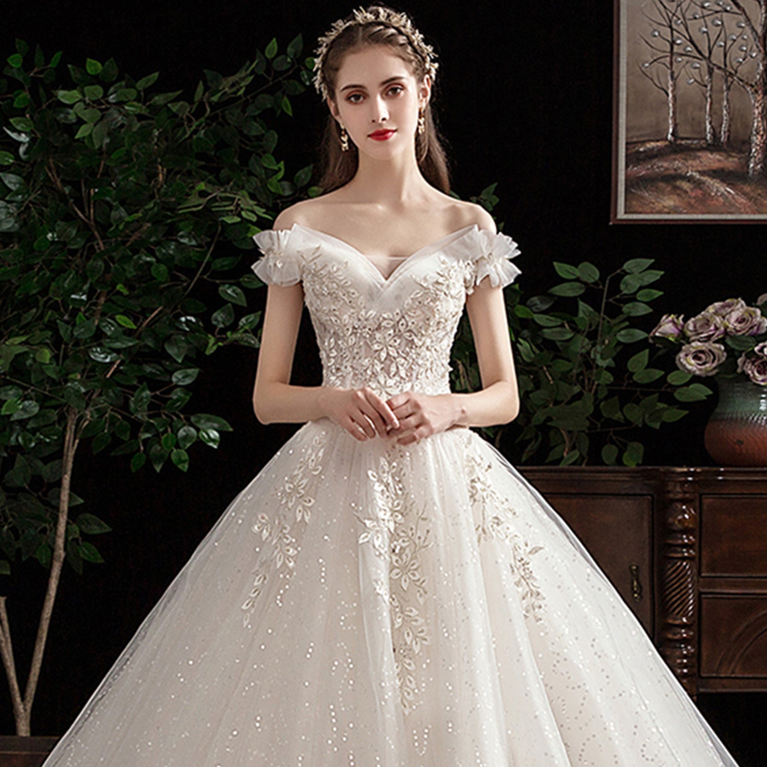 Editorial bridal model wearing a glittering off-the-shoulder V-neck princess bridal gown paired with a delicate gold floral crown tiara.