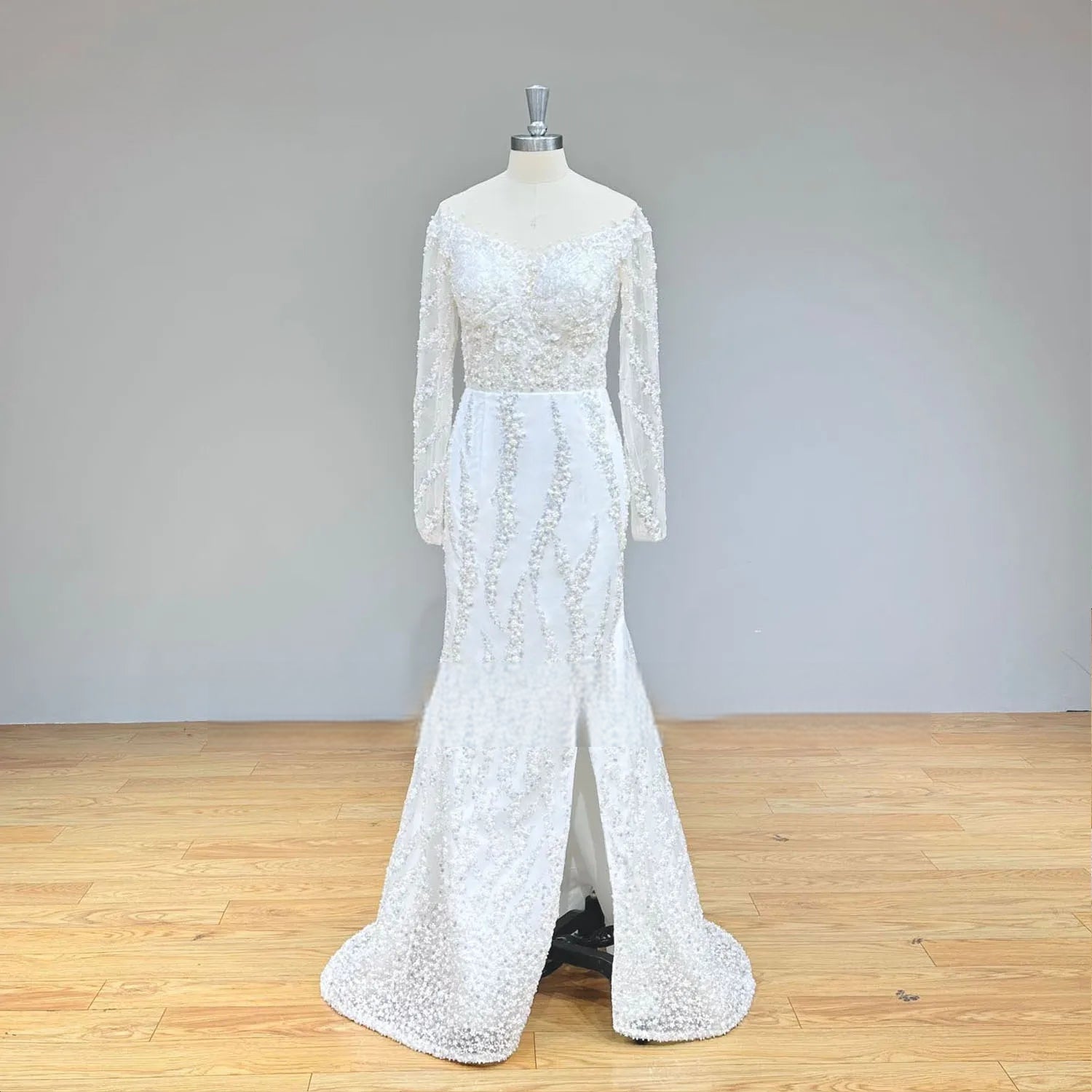 Front view of an elegant model wearing a white shiny beaded ball gown wedding dress with long sleeves and shimmering sequin patterns in a luxury bridal showroom.