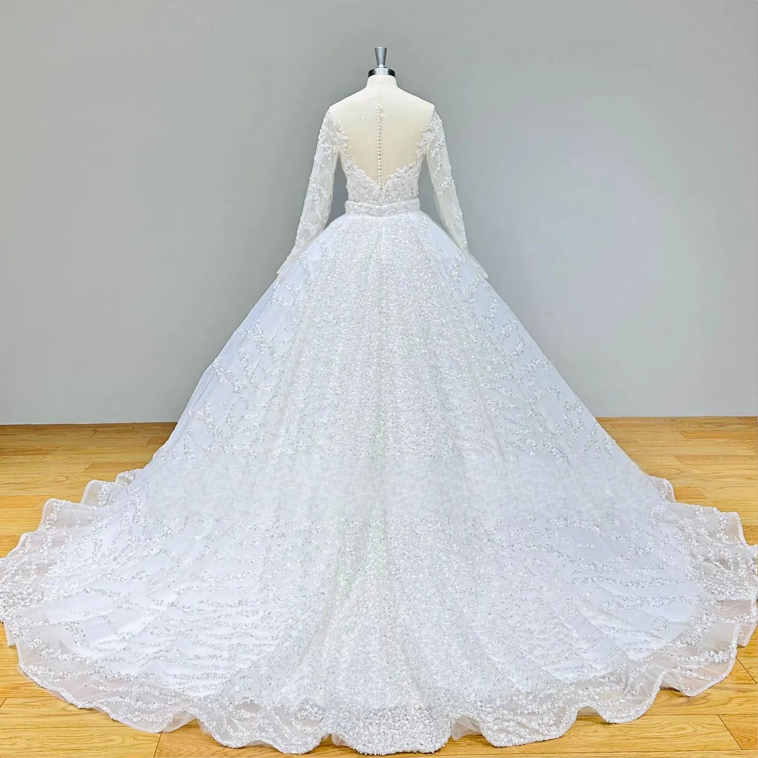 Wide rear view of the shiny beaded long sleeve ball gown wedding dress on a mannequin, emphasizing the grand scale of the sequined cathedral train.