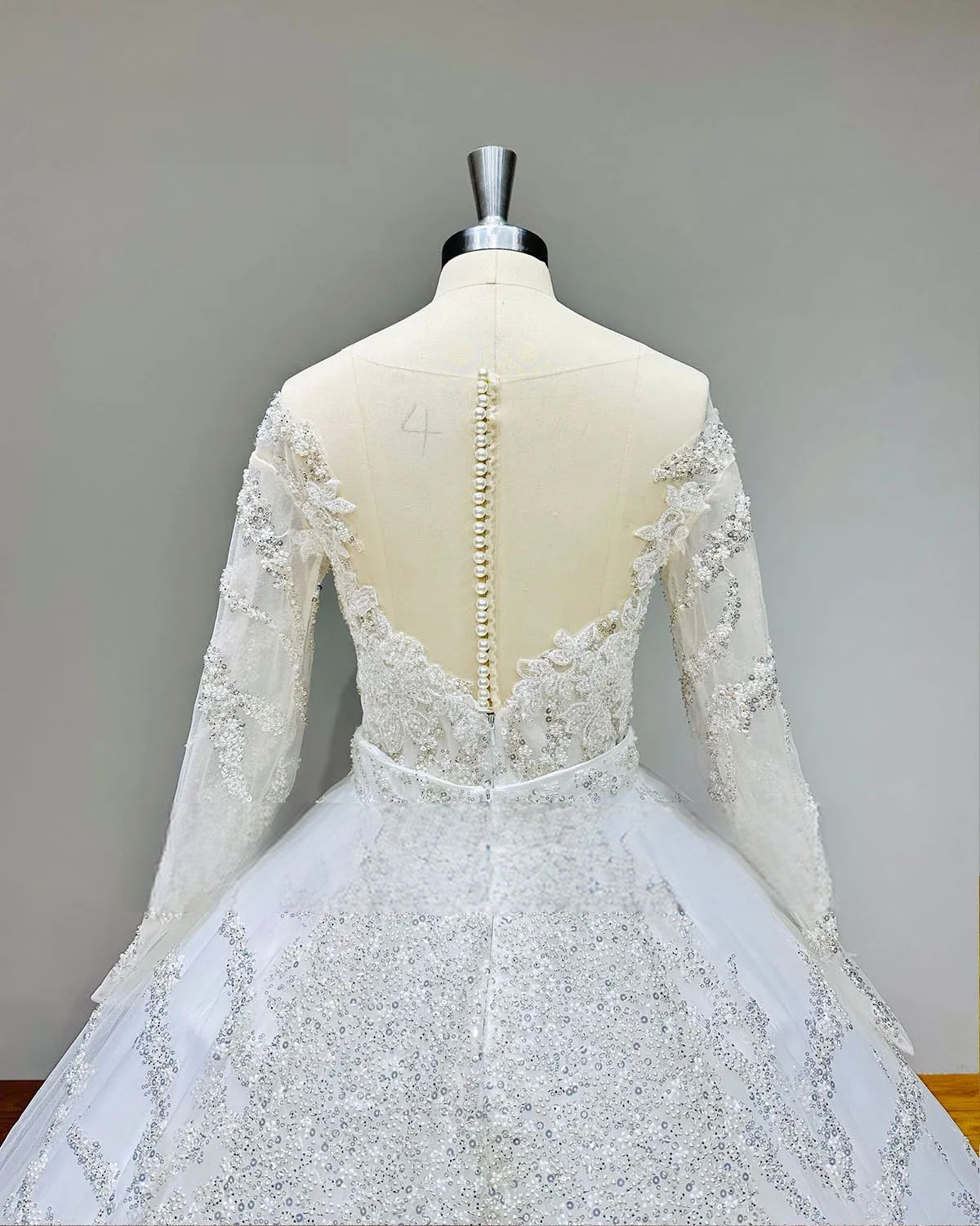 Wide rear view of the shiny beaded long sleeve ball gown wedding dress on a mannequin, emphasizing the grand scale of the sequined cathedral train.