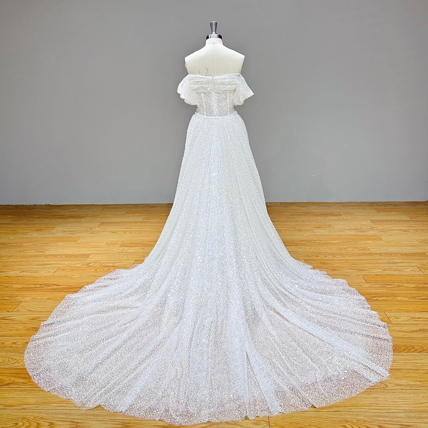 Full-length back studio view of a dazzling white sequin and bead-embellished tulle mermaid wedding gown on a mannequin without the overskirt.