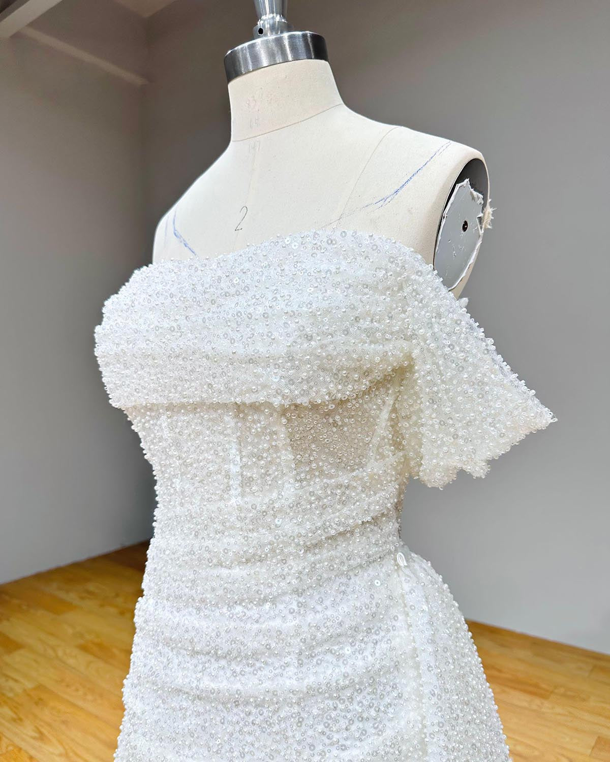 Close-up front view of a couture wedding dress bodice highlighting heavy sequined beading, pearl embellishments, and structured sheer corset boning.