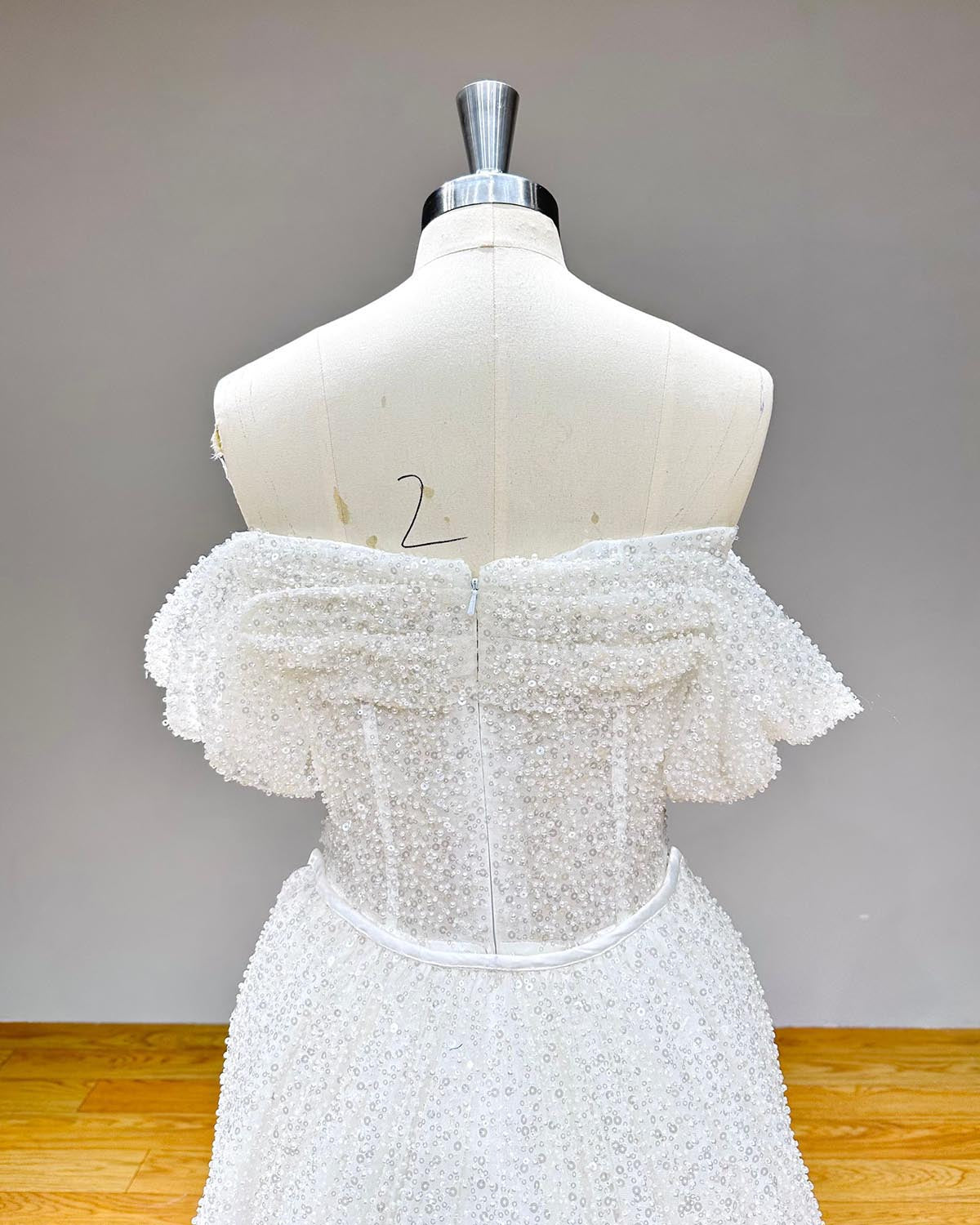 Detailed back view of a glittering off-the-shoulder wedding gown bodice showcasing a seamless zipper closure and dense all-over sequin work.