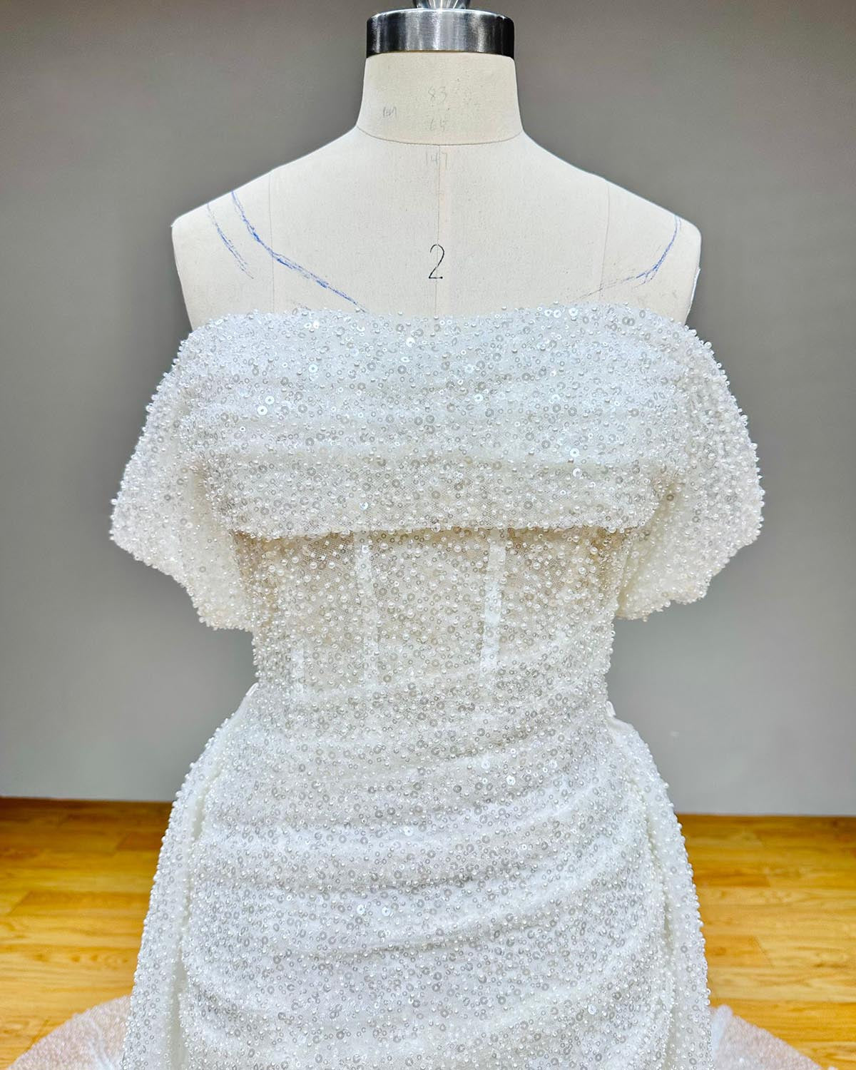 Macro studio shot of a white wedding dress bodice detailing the heavily encrusted pearl and sequin textures along a cuffed portrait collar.