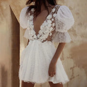 Whimsical short backless wedding dress with a deep plunging V-neckline, sheer illusion bodice, 3D floral appliques, and pearl-beaded half puff sleeves.