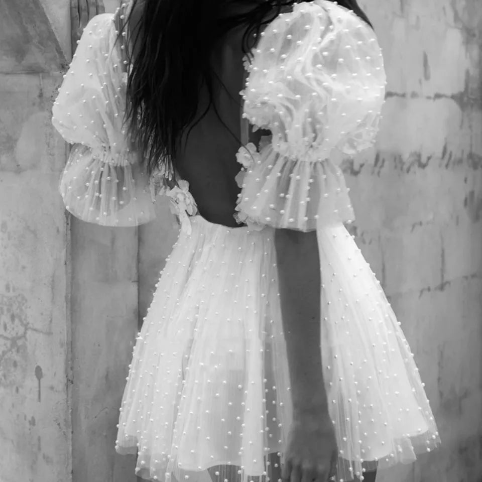 Black and white rear profile view of a sexy backless short bridal gown highlighting a low open back cut and voluminous tulle puff sleeves dotted with pearls
