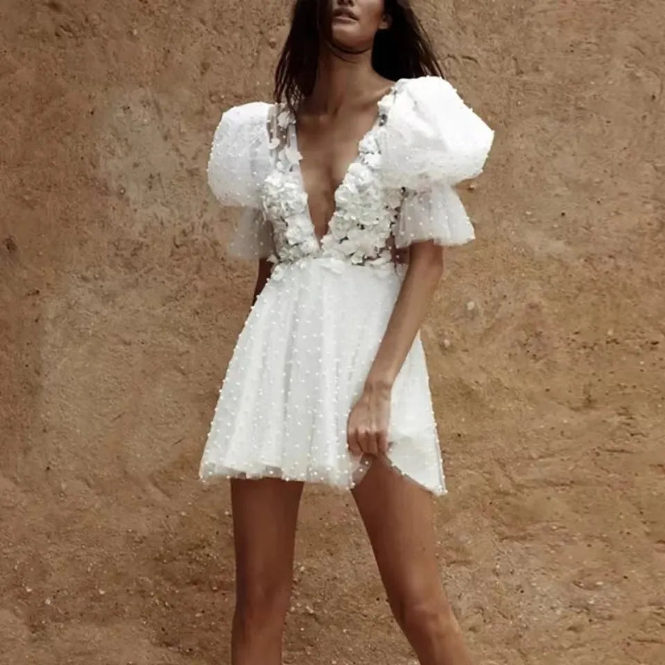 Avant-garde short ivory bridal dress with cascading 3D flower elements across a sheer mesh bust and a tiered tulle mini skirt, styled in an outdoor setting.