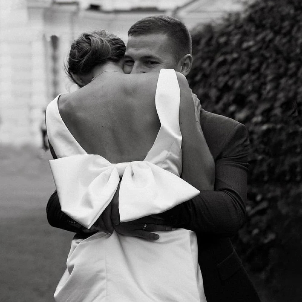 Close-up rear view of a sexy backless satin bridal dress highlighting a plunging low V-cut back accented with a large structured statement bow.