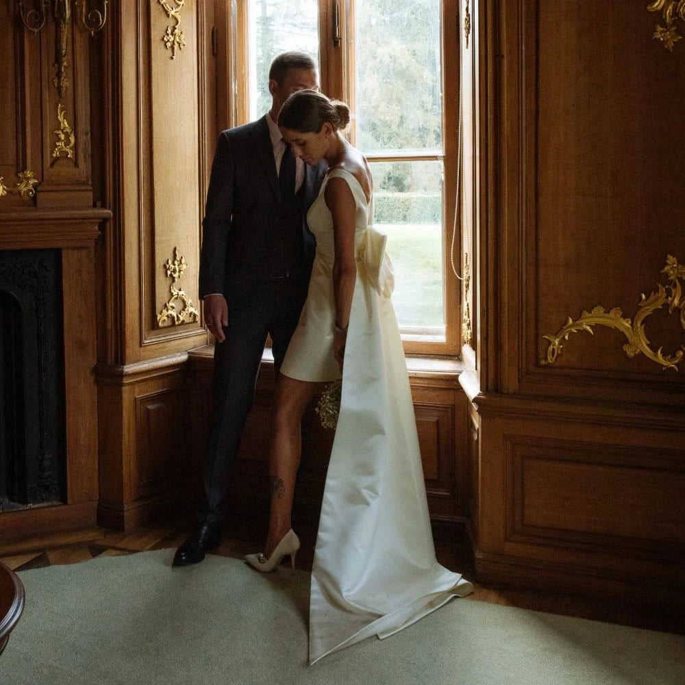 Minimalist sleeveless short satin sheath dress with an attached long back train extension, captured in a luxury estate setting.
