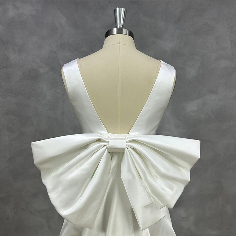 Studio close-up of a low-cut backless satin bridal gown on a mannequin, emphasizing the precise craftsmanship of a wide structured oversized back bow