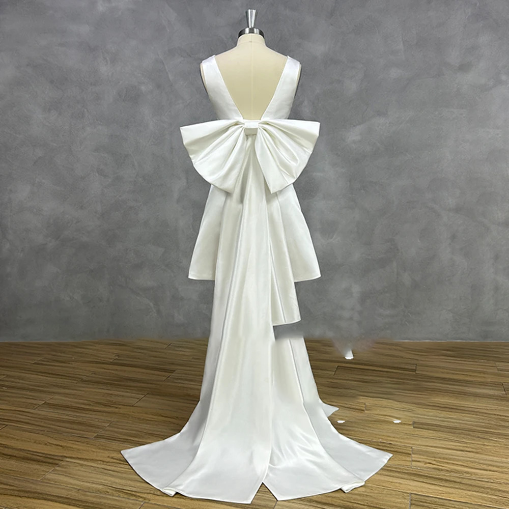 Full rear view of a 2-in-1 short satin wedding gown on a mannequin, displaying the deep open back layout with a grand detachable bow and a sweeping floor-length train.
