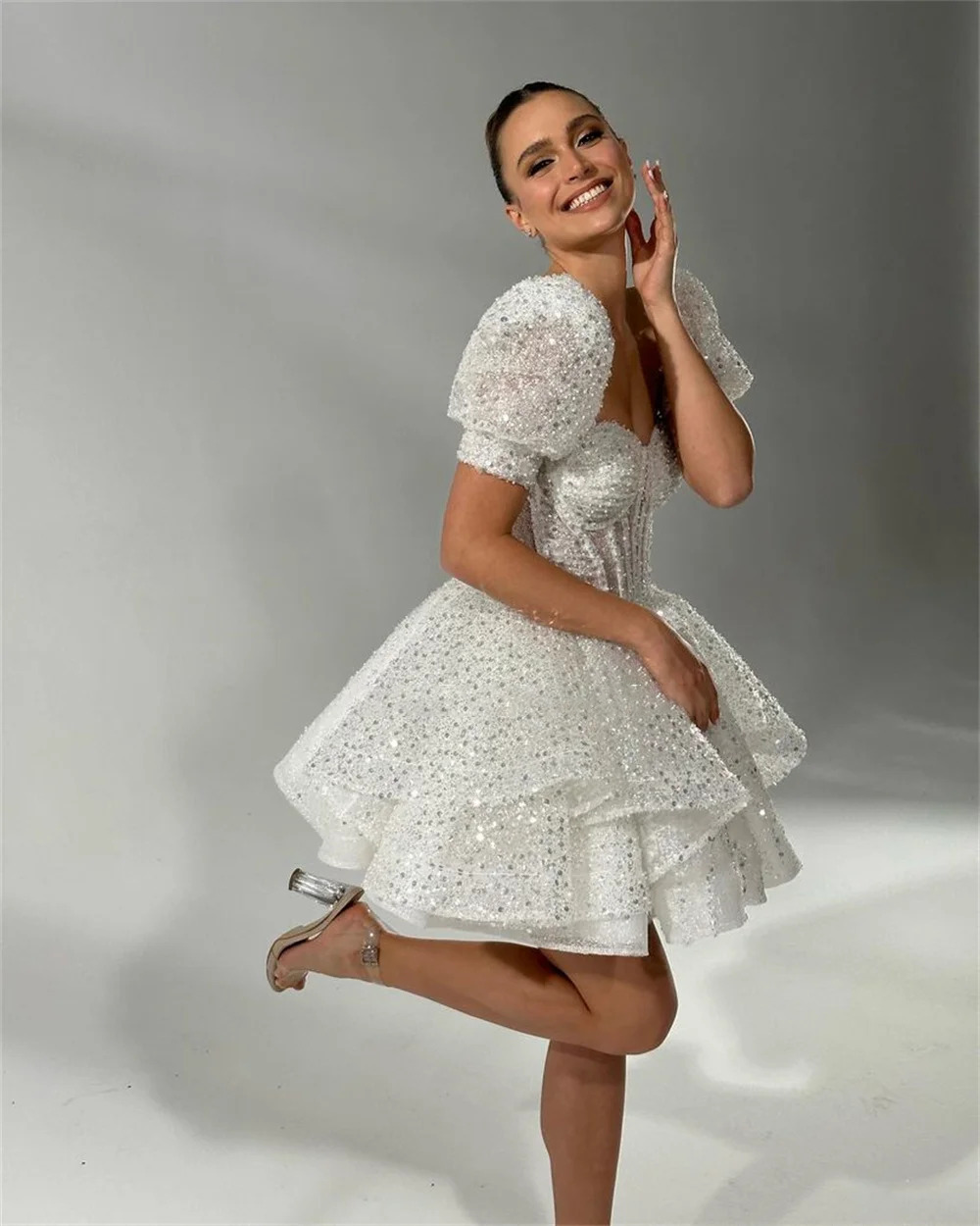 Side view of a sparkling white mini bridal gown with short puff sleeves and a flirty tiered tulle princess skirt, styled for a reception party.