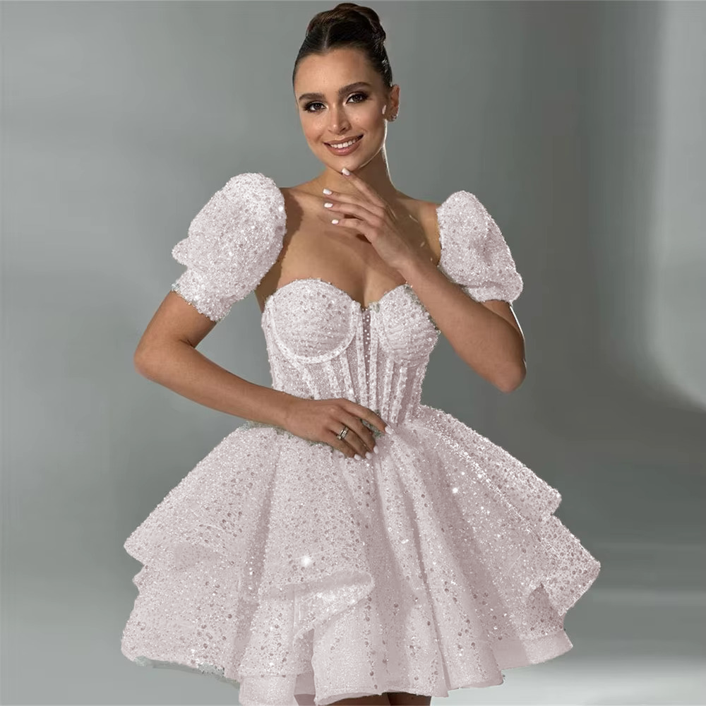 Romantic soft pink short homecoming or party dress with sequined details, short puff sleeves, and a tiered ruffle princess mini skirt.