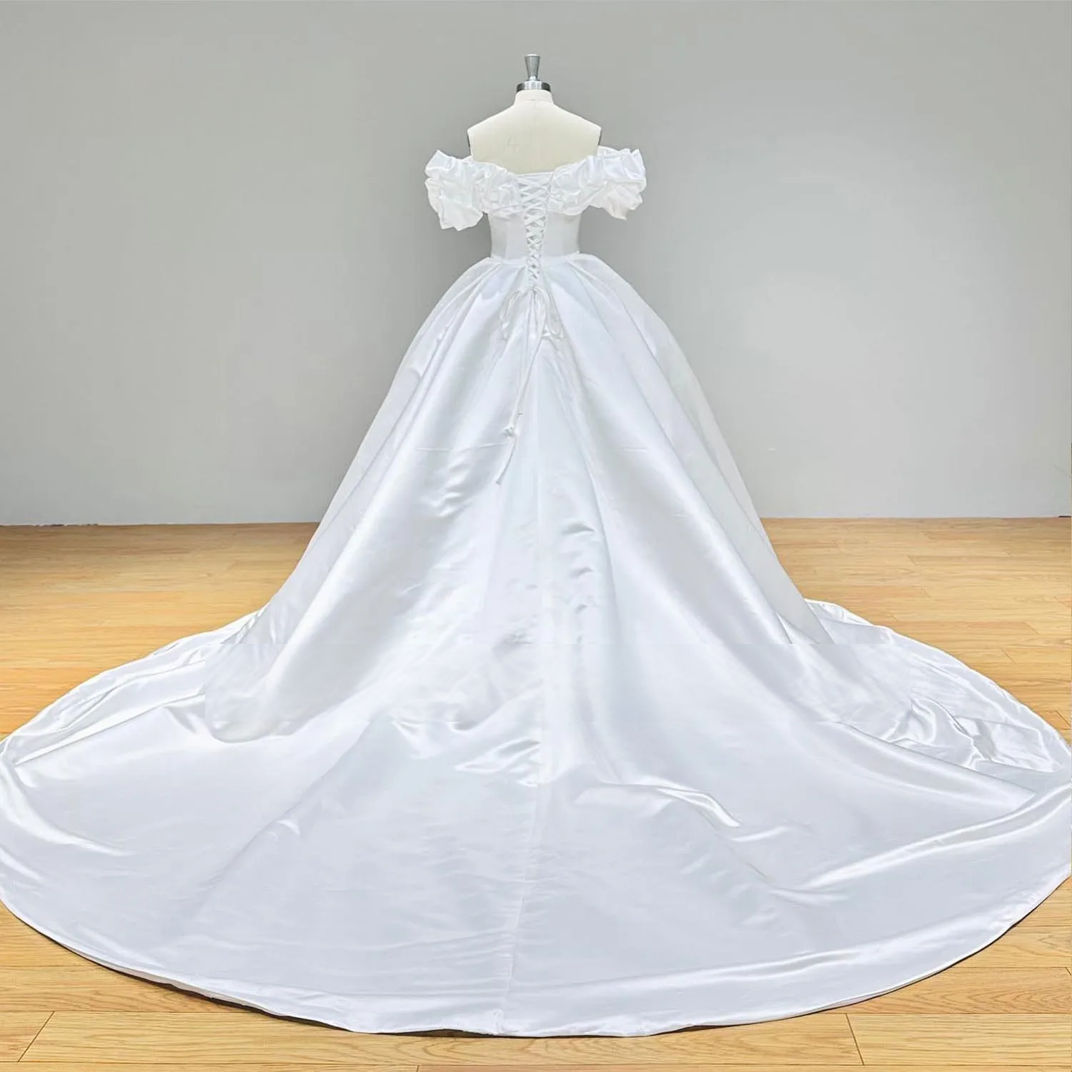 Back view of a satin ball gown wedding dress on a mannequin, highlighting the elegant lace-up corset back and sprawling cathedral train.