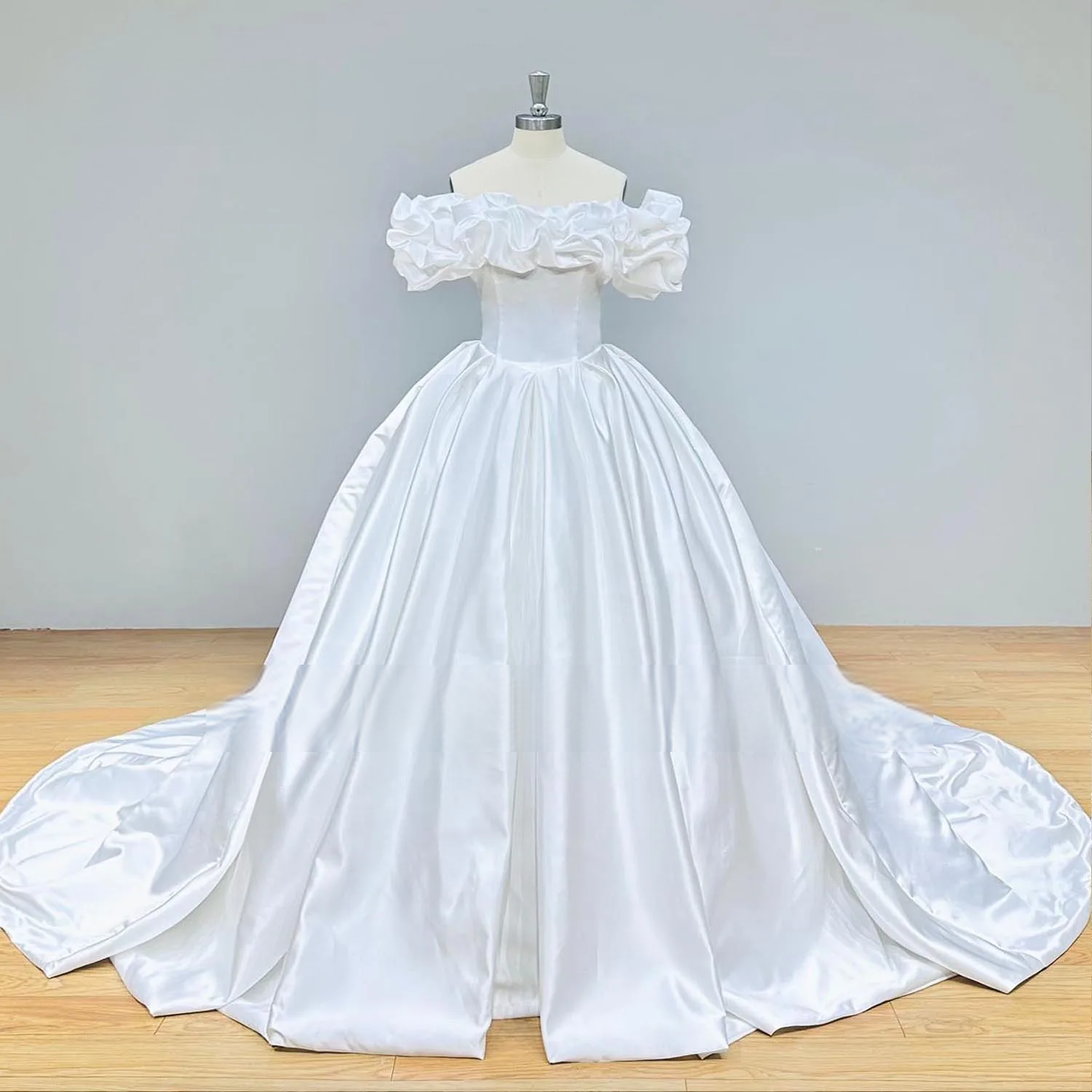 Simple front view of a matte satin ball gown bridal dress on a mannequin, showcasing the unique ruffled off-the-shoulder design and full-length train.