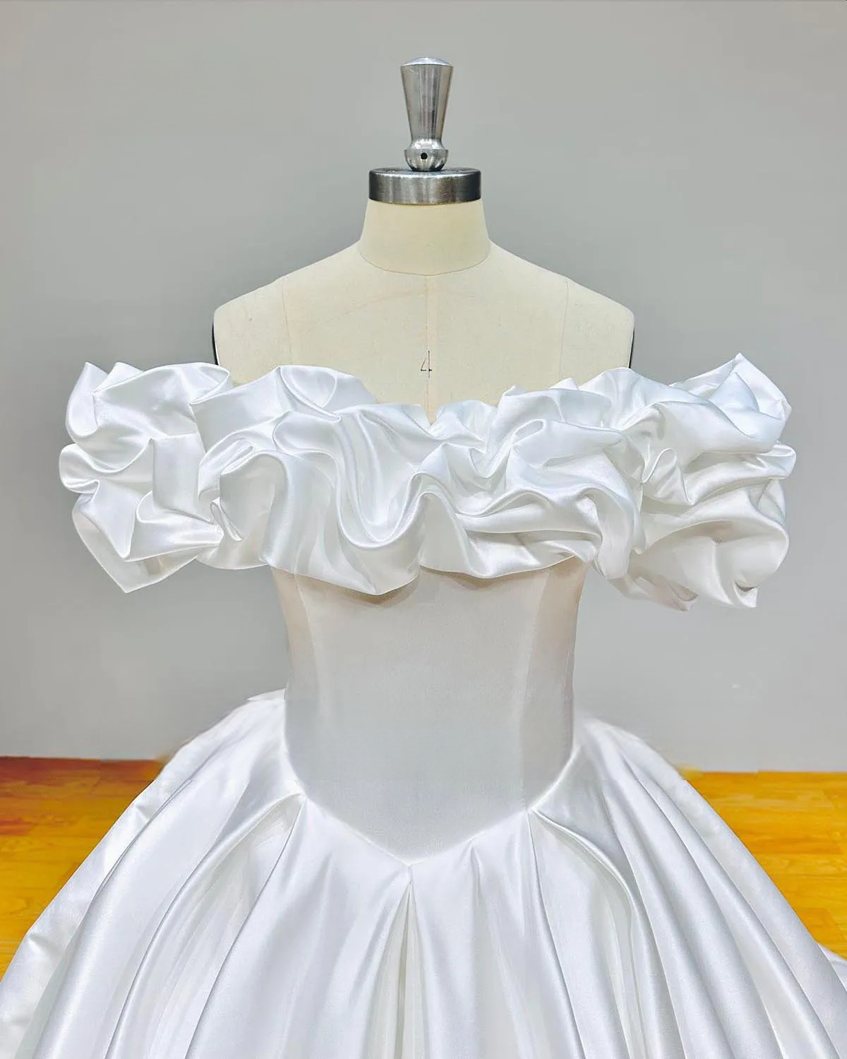Detailed close-up of the oversized ruffled off-the-shoulder neckline and smooth matte satin bodice of a luxurious ball gown wedding dress.