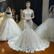 Front view of an elegant model wearing a simple beach-style light mermaid wedding dress with an illusion plunging neckline, delicate lace cap sleeves, and a flowy train.