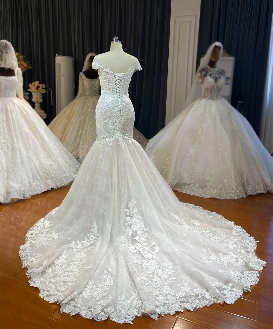 A three-quarter back angle of the simple beach-style bridal gown, showing the fitted silhouette, corset back, and the spread of the flowy lace train.