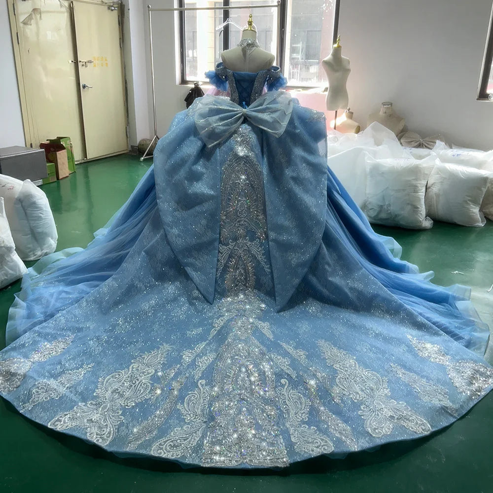 Full back view of a light blue ball gown on a mannequin, featuring a large structural statement bow at the waist and a grand cathedral train with intricate silver lace borders.