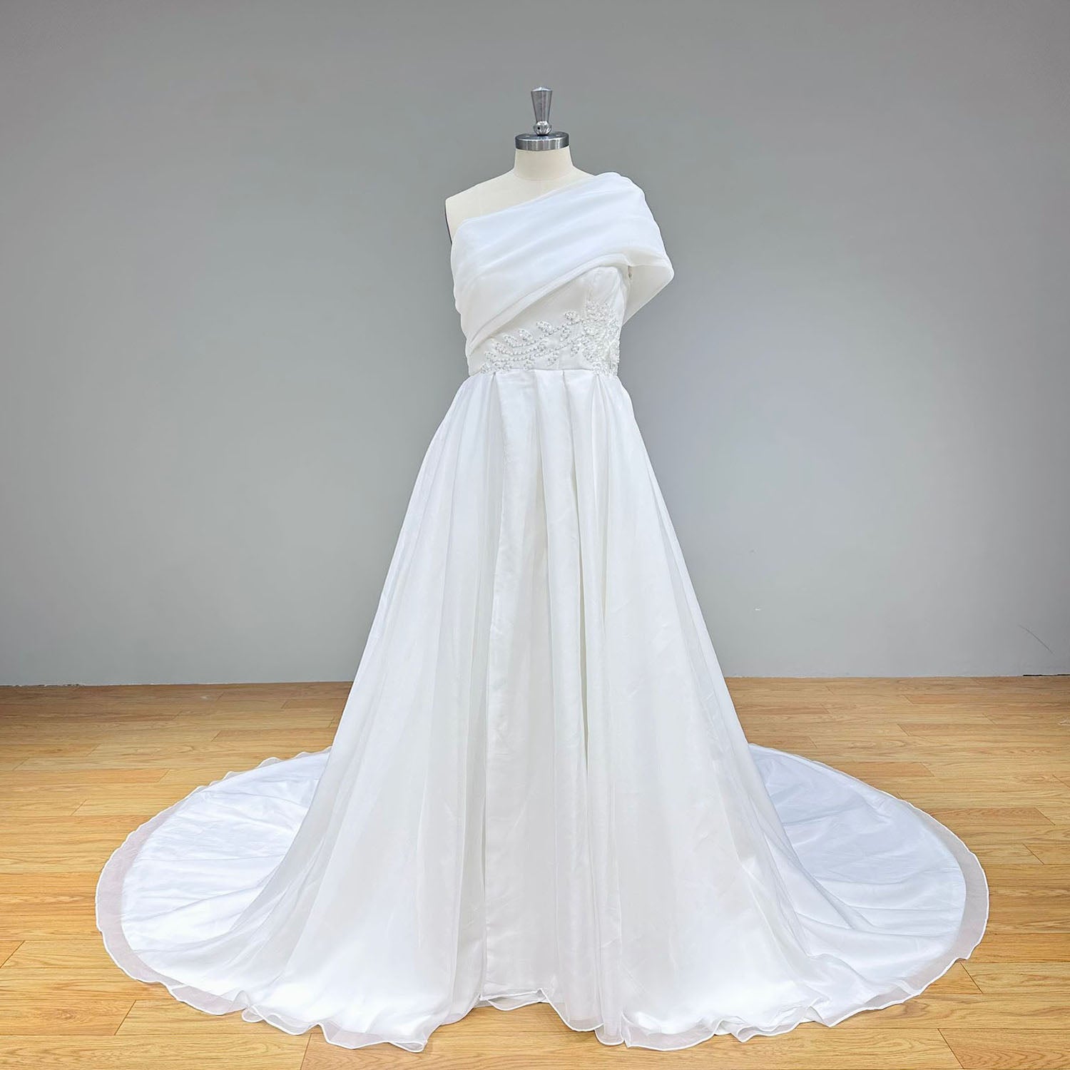 Full-length front perspective of the elegant white organza bridal dress with an asymmetrical neckline and embroidered waist detailing, shown on a mannequin.