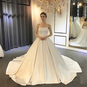 Front view of an elegant mermaid wedding dress featuring intricate white lace appliques over a champagne-colored base, long illusion sleeves, and a voluminous detachable overskirt.