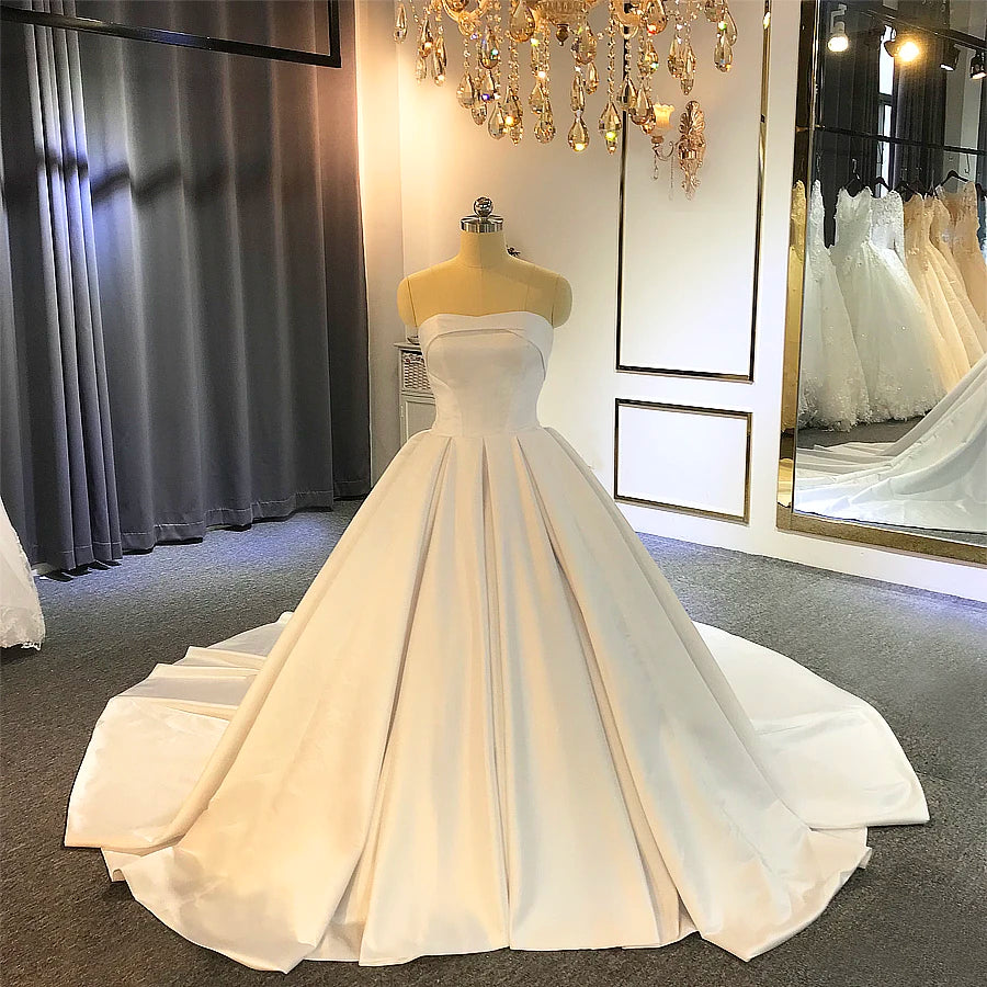 Front perspective of a simple white satin ball gown wedding dress on a mannequin, highlighting the elegant strapless neckline and voluminous pleated skirt.