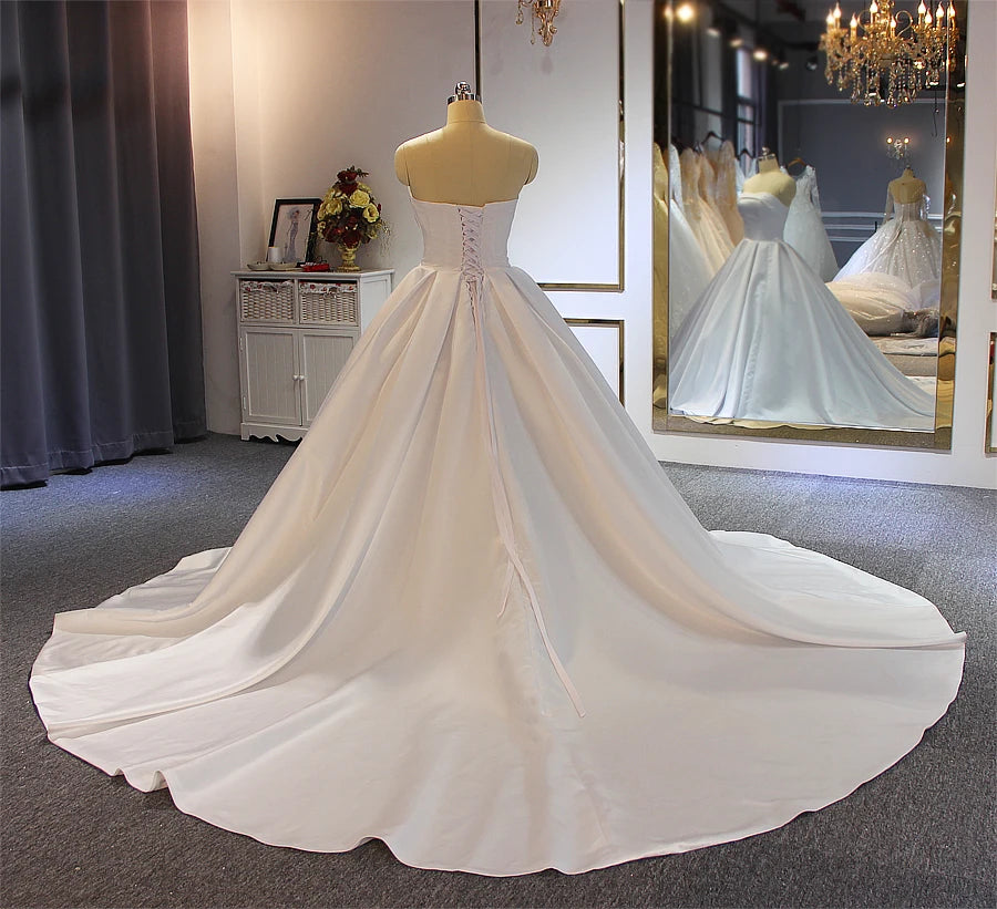 Rear view of a simple satin bridal gown on a mannequin, displaying a traditional lace-up corset back and a beautiful sweeping floor-length train.