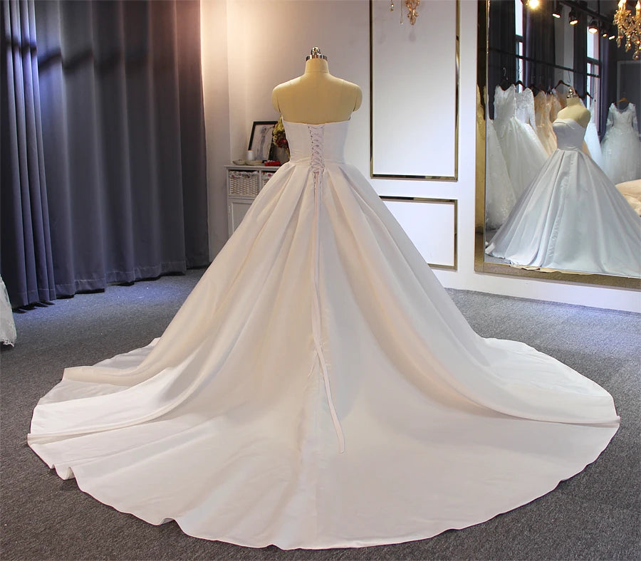 Full back perspective of an affordable luxury satin wedding dress, emphasizing the classic corset closure and the expansive circular sweep of the elegant train.