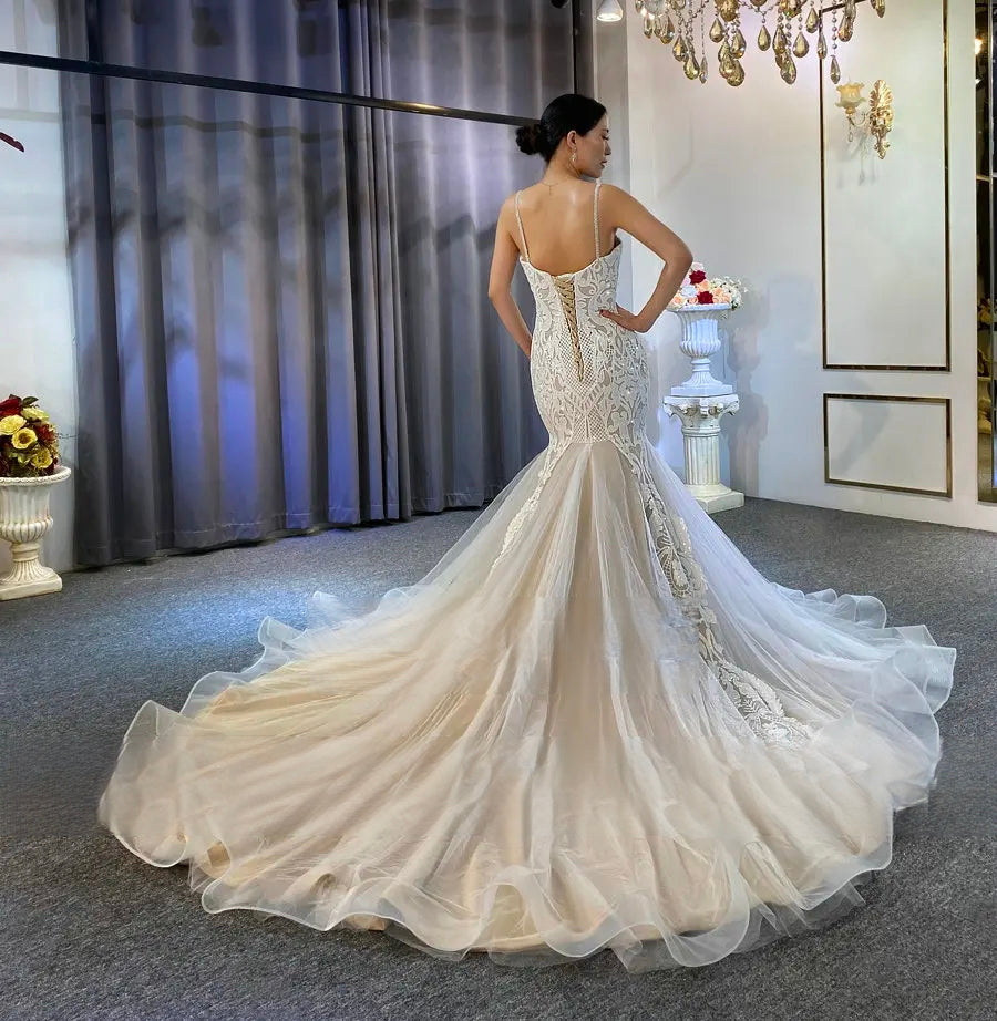 Detailed back shot of a slim wedding dress highlighting the elegant corset closure and the transition from the fitted lace bodice to a voluminous flared train.
