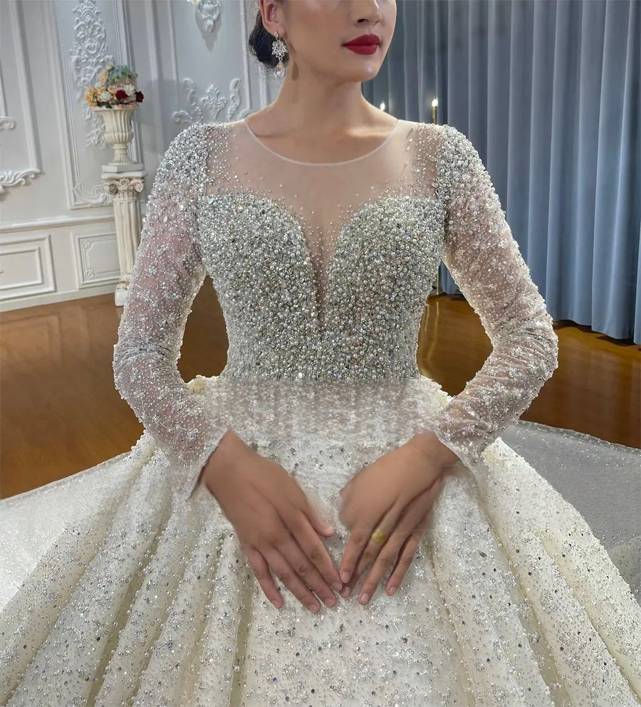 Close-up of the elegant wedding gown bodice, highlighting the intricate heavy crystal beading, sheer long sleeves, and a plunging illusion neckline.