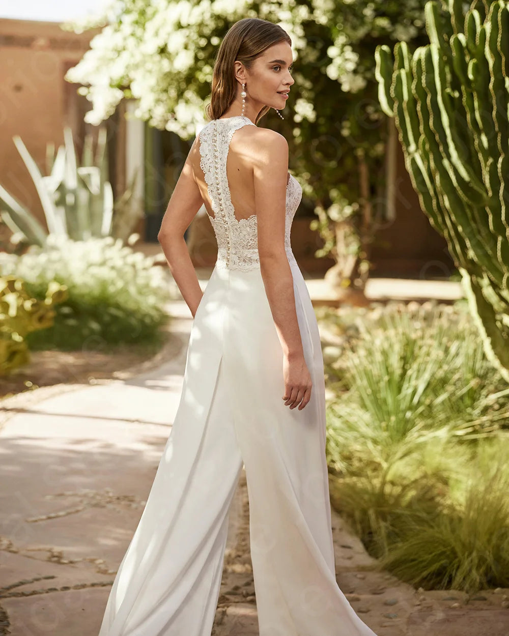 Rear three-quarter view of the elegant lace bridal pantsuit, highlighting the sophisticated open back bordered with intricate floral lace appliques and high-waisted trousers.