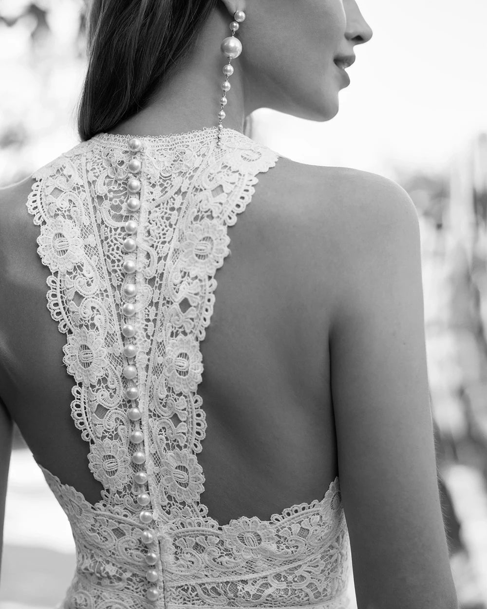 Close-up black and white photograph focusing on the fine lace details and delicate button-down spine closure of the high neck halter wedding jumpsuit bodice.