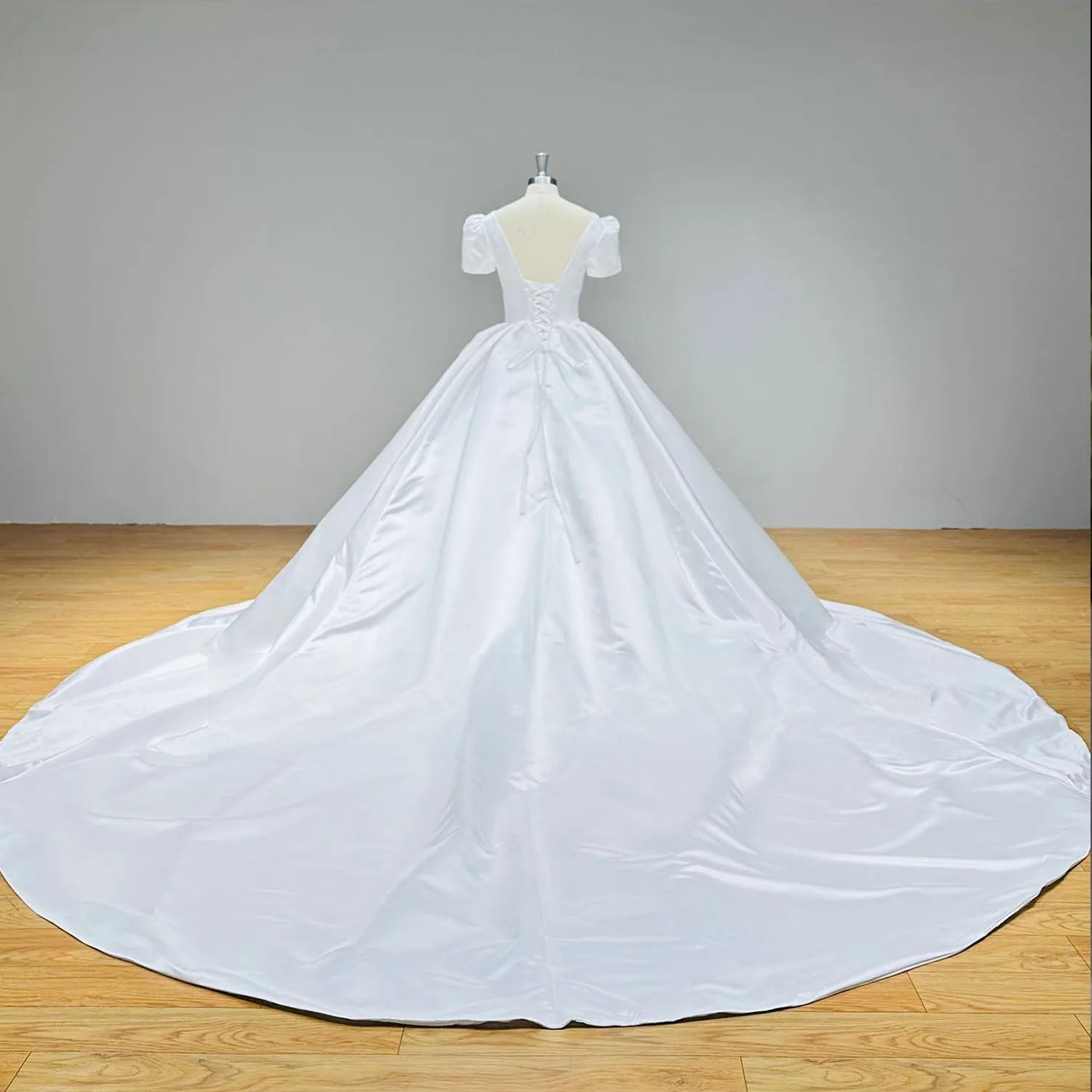 Detailed back view of a satin bridal gown on a mannequin, showcasing the traditional lace-up corset back and the beginning of a sweeping cathedral train.