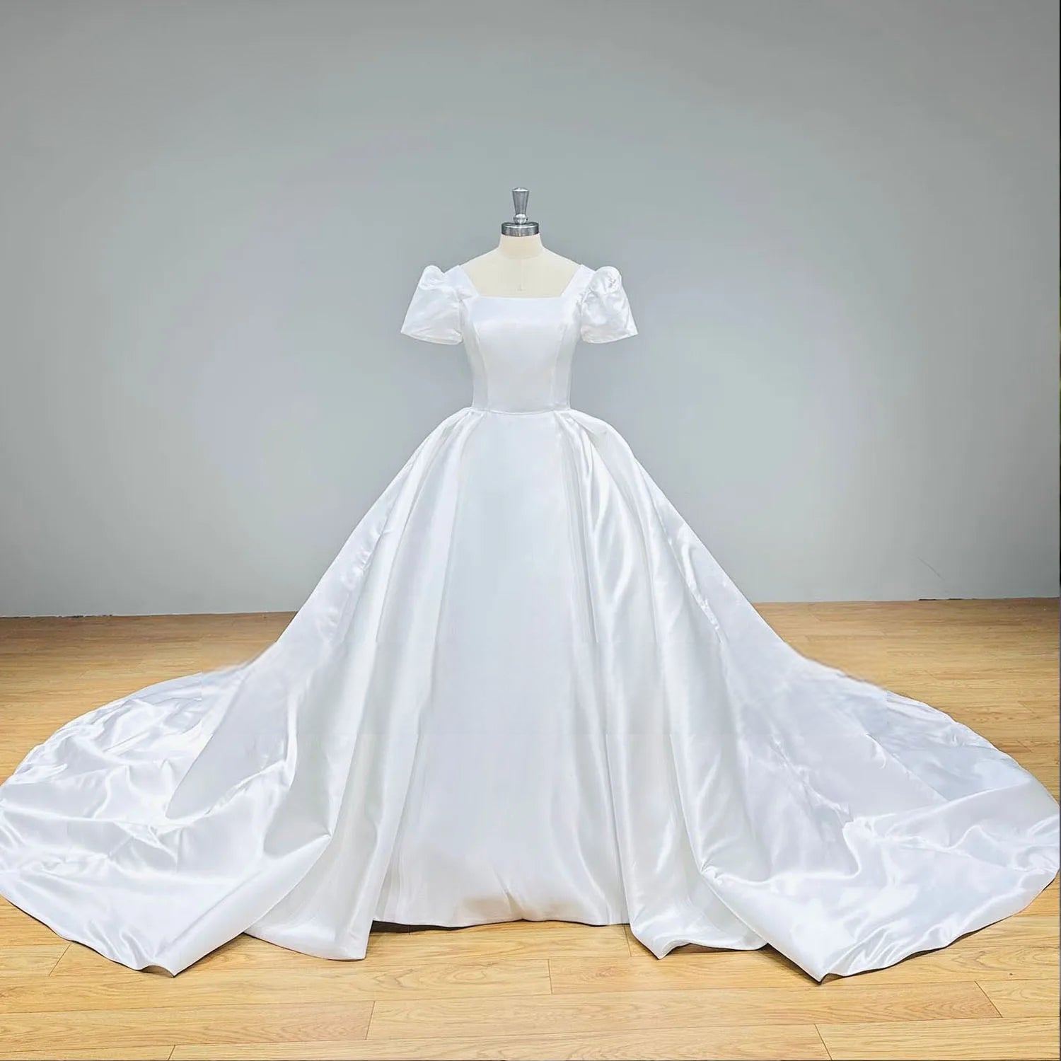 Studio front view of a minimalist satin ball gown bridal dress with a structured square neck bodice and short puffed sleeves on a professional mannequin.