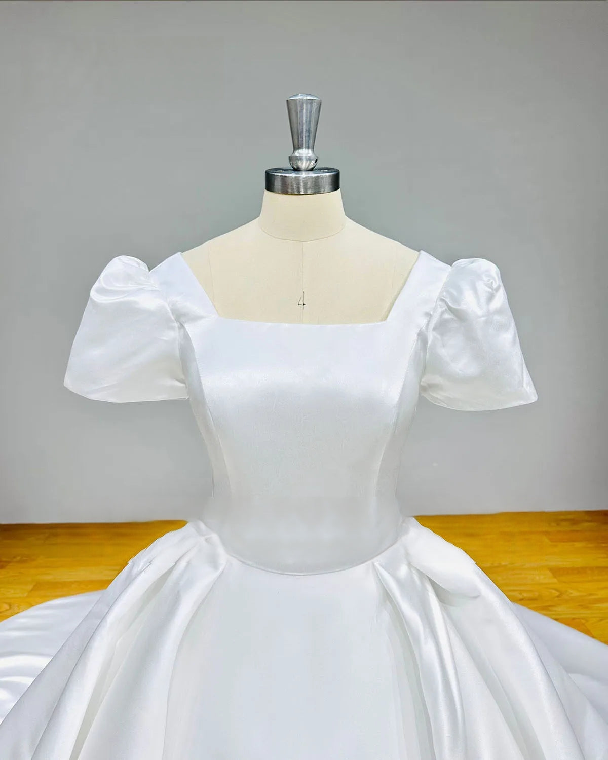 Close-up detail of a white satin wedding dress bodice featuring a modern square neckline and elegant short sleeve tailoring for a timeless bridal look.