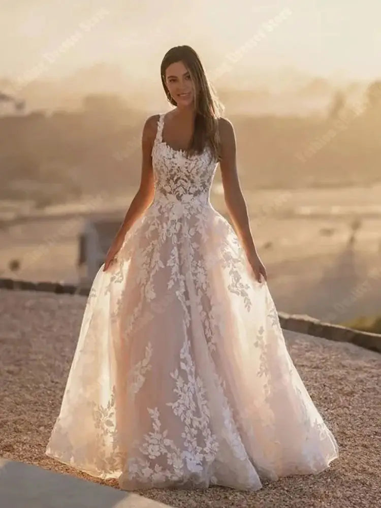 A bride in a sleeveless square-neck wedding dress with a shining tulle surface, posing elegantly against a sunset background.