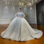 Full-length front view of a luxury square neckline long sleeve sparkly ball gown wedding dress with an expansive sequined skirt and shimmering silver details in a grand bridal showroom.