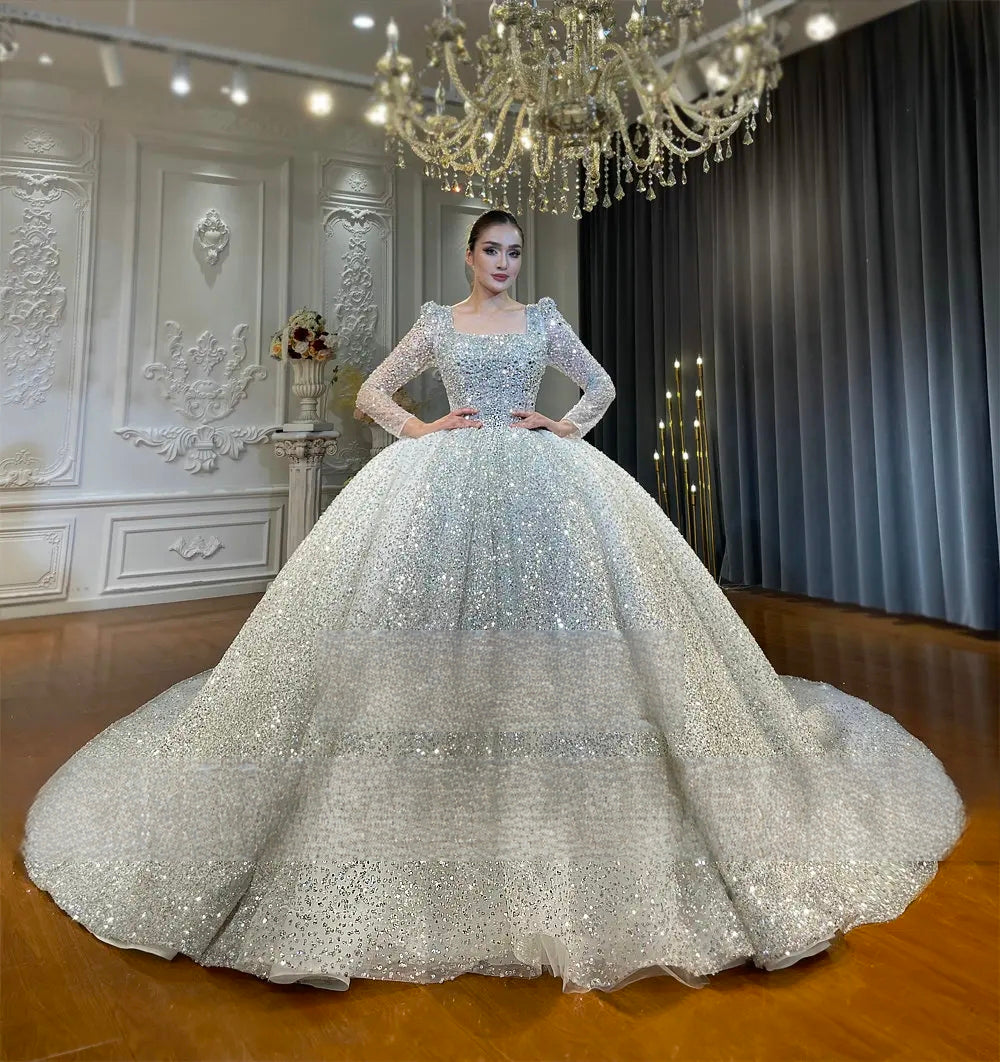 Elegant front perspective of a shimmering silver sequin bridal gown featuring a square neckline, long sleeves, and a voluminous ball gown silhouette.