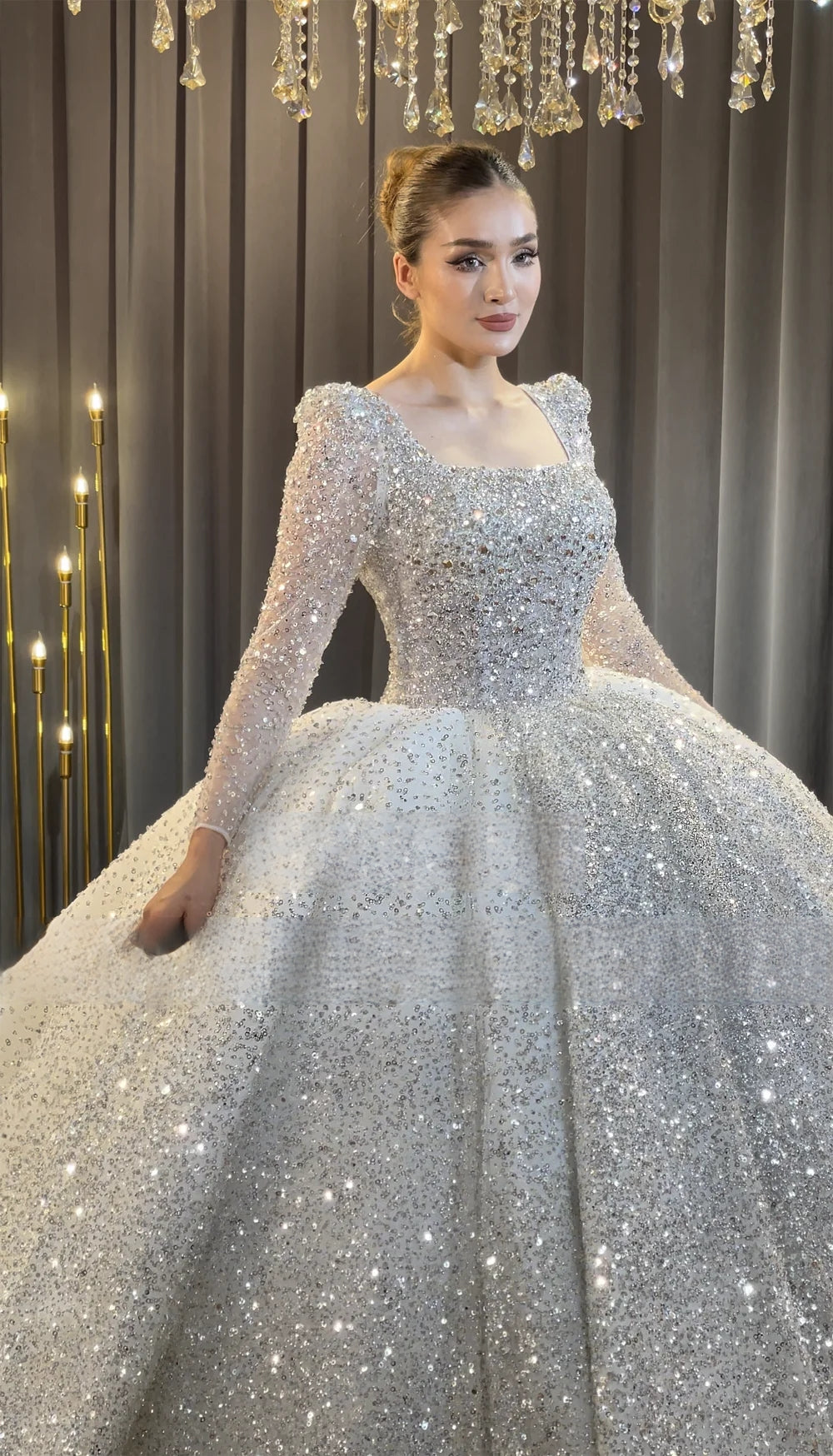Close-up of the square neckline and long sleeves on a sparkly bridal gown bodice, highlighting the dense, handcrafted silver sequin embellishments.