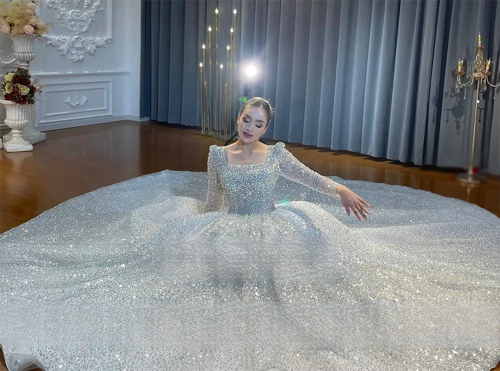 Dramatic wide shot of a massive sparkly ball gown wedding dress spread in a full circle around the bride, emphasizing the grand scale and brilliance of the sequined fabric.