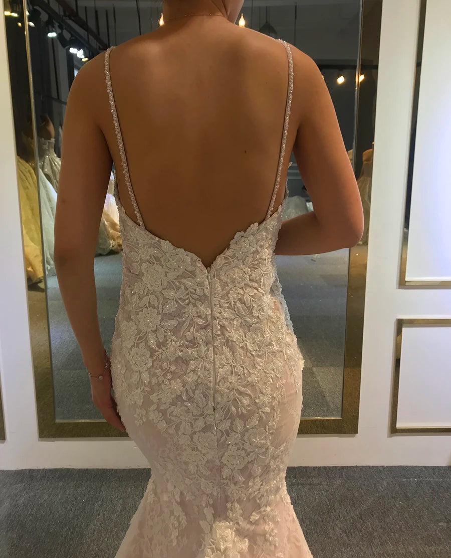 Close-up of the back of a patterned lace mermaid bridal gown showcasing thin spaghetti straps, a low back design, and intricate floral lace detailing.