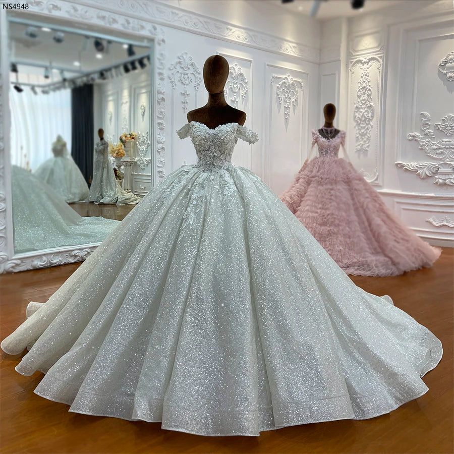 Front-facing view of an elegant off-the-shoulder wedding dress with a voluminous sparkling ball gown skirt.
