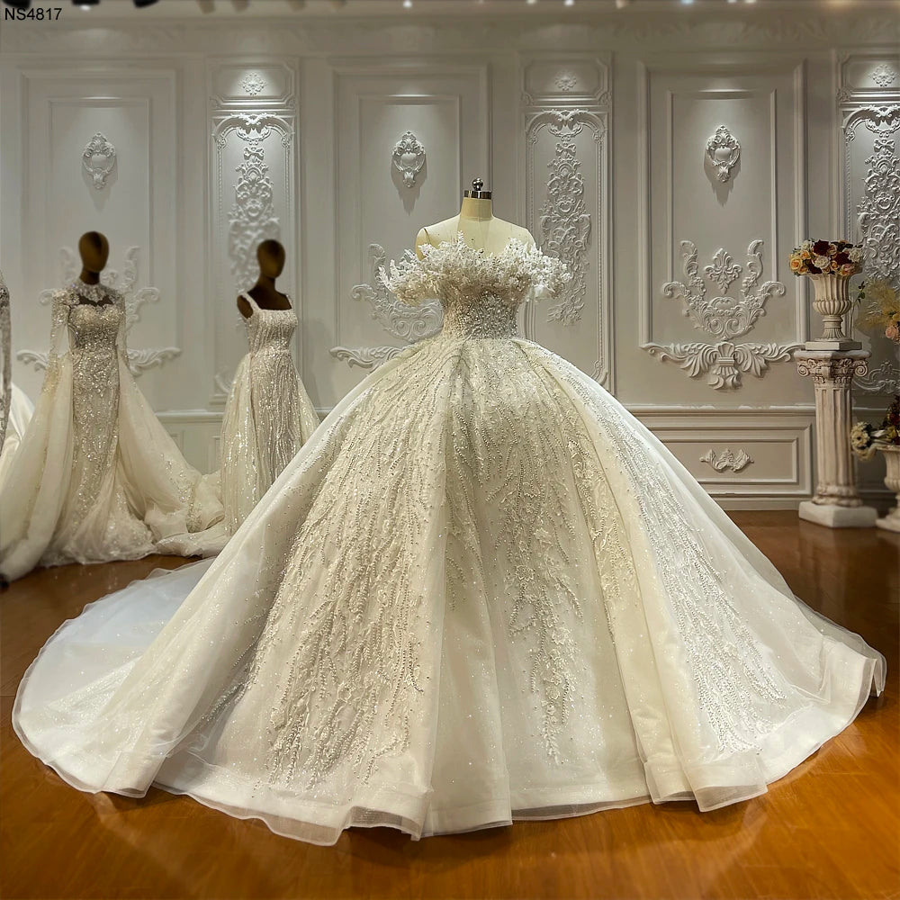 Full front view of a luxury off-the-shoulder ball gown wedding dress on a mannequin, featuring intricate lace appliqués and a voluminous shimmering skirt in a professional bridal studio.