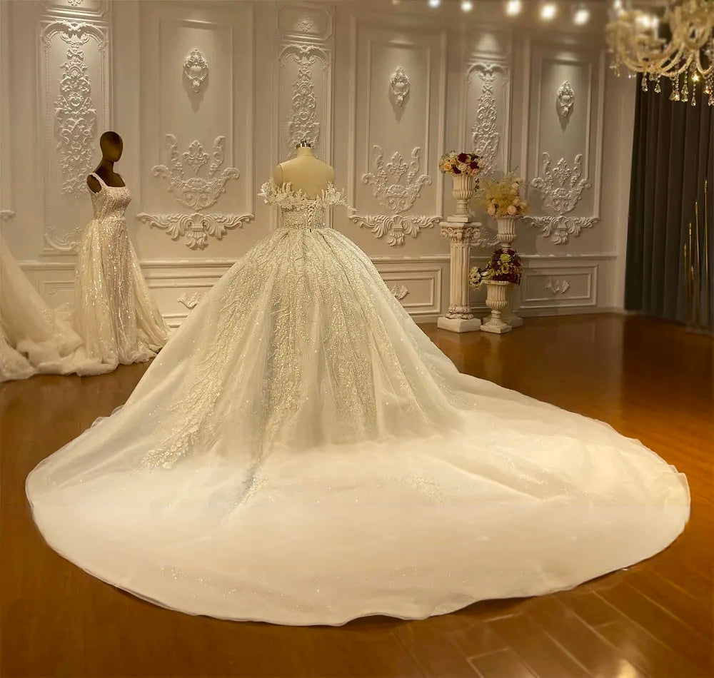 Back view of a strapless bridal ball gown highlighting an expansive shimmering cathedral train with delicate lace detailing and a royal silhouette.