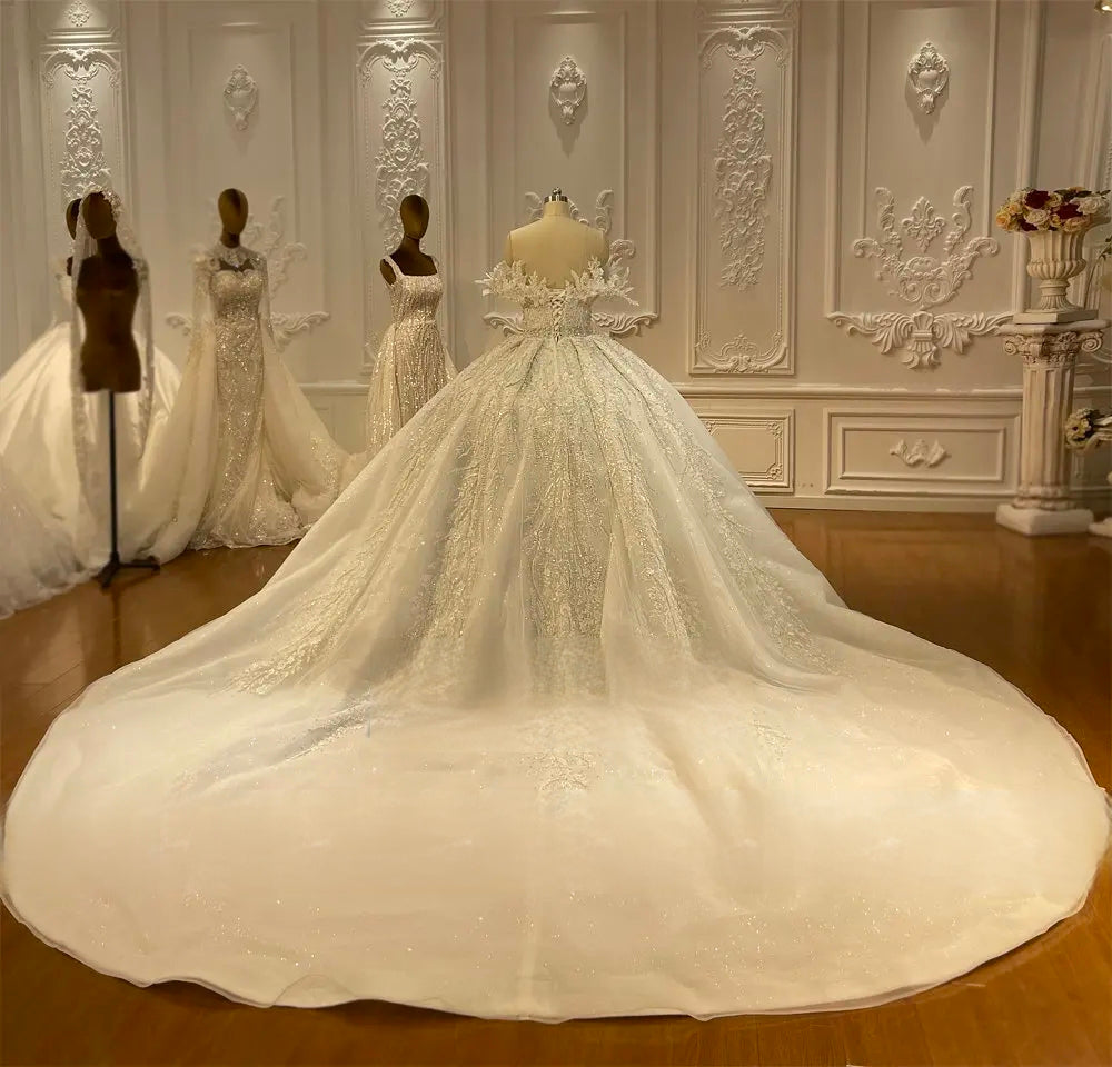 Rear profile of a strapless off-the-shoulder wedding dress featuring a lace-up back and a majestic wide-sweep circular train with glitter-patterned lace.