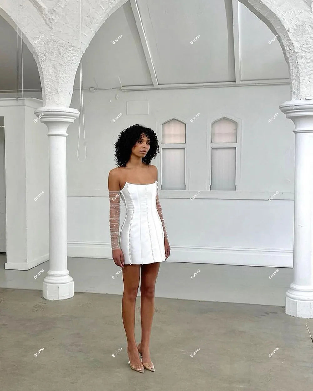 Full-length studio view of a modern white strapless mini dress for brides, featuring refined boning, pearl detailing, and long sheer mesh gloves.
