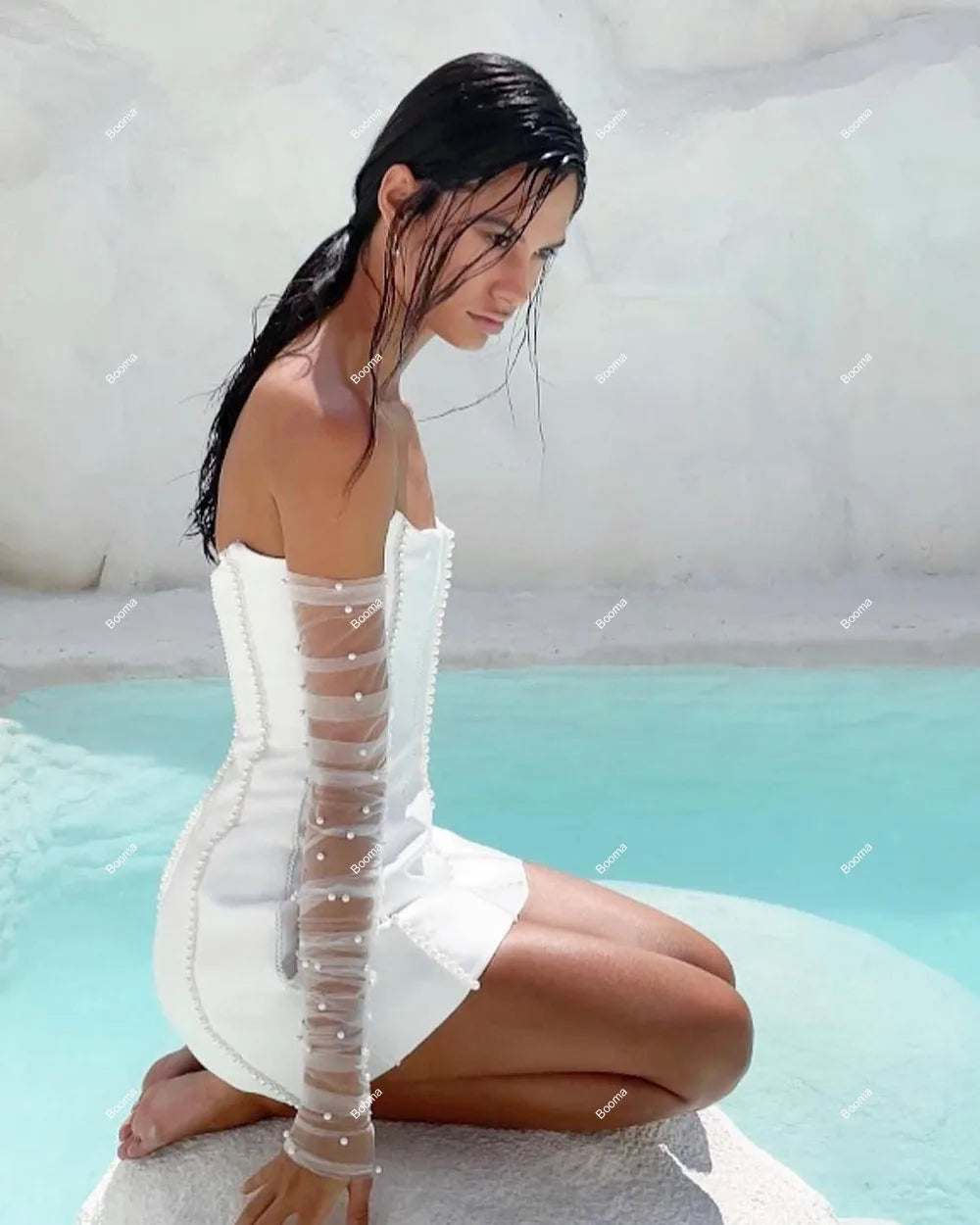 Artistic side profile of a bride in a white strapless mini dress with pearl-embellished sleeves, posing near a pool.