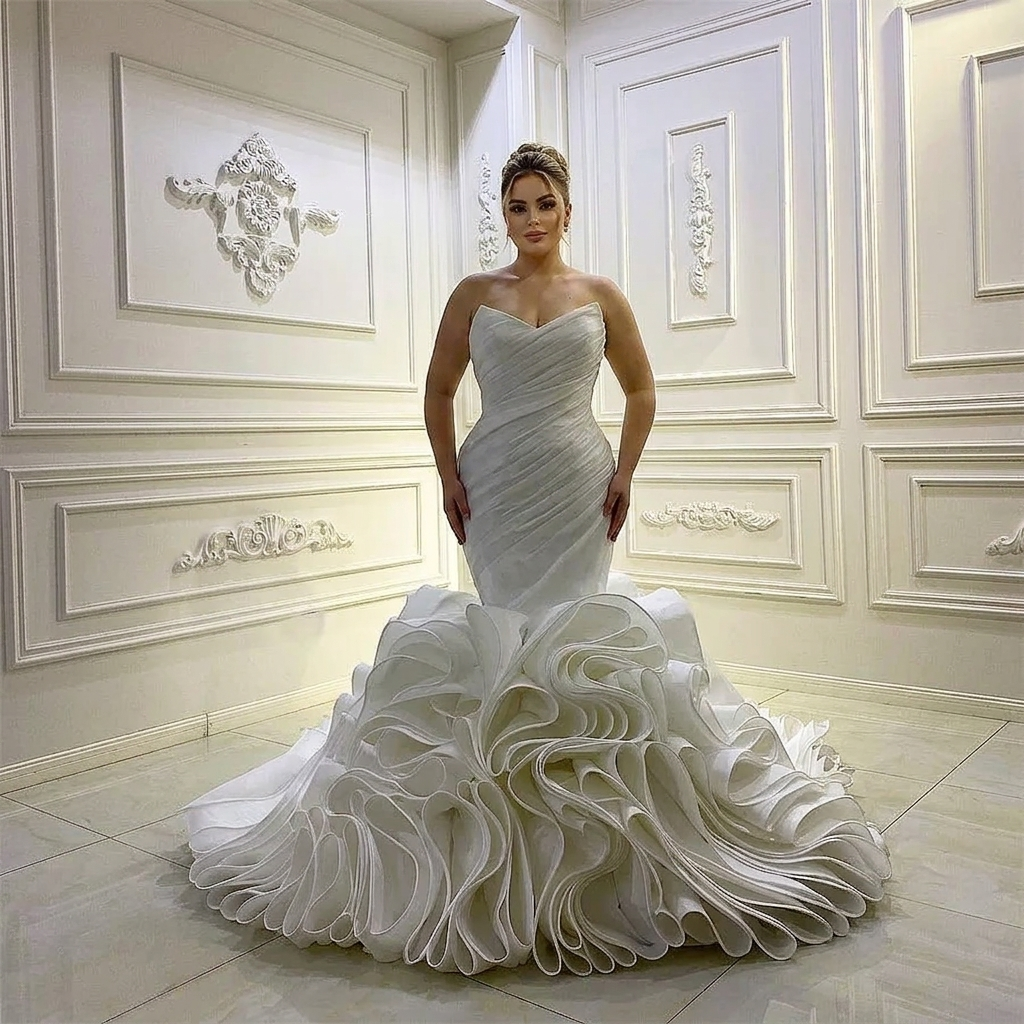 Full-length perspective of a brunette model posing in an elegant strapless trumpet bridal gown featuring a dramatic large ruffle bottom in an ornate white room.